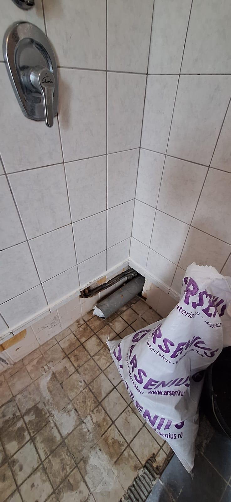 Badkamerrenovatie in uitvoering: leidingen en thermostaatkraan zichtbaar na verwijderen tegels.