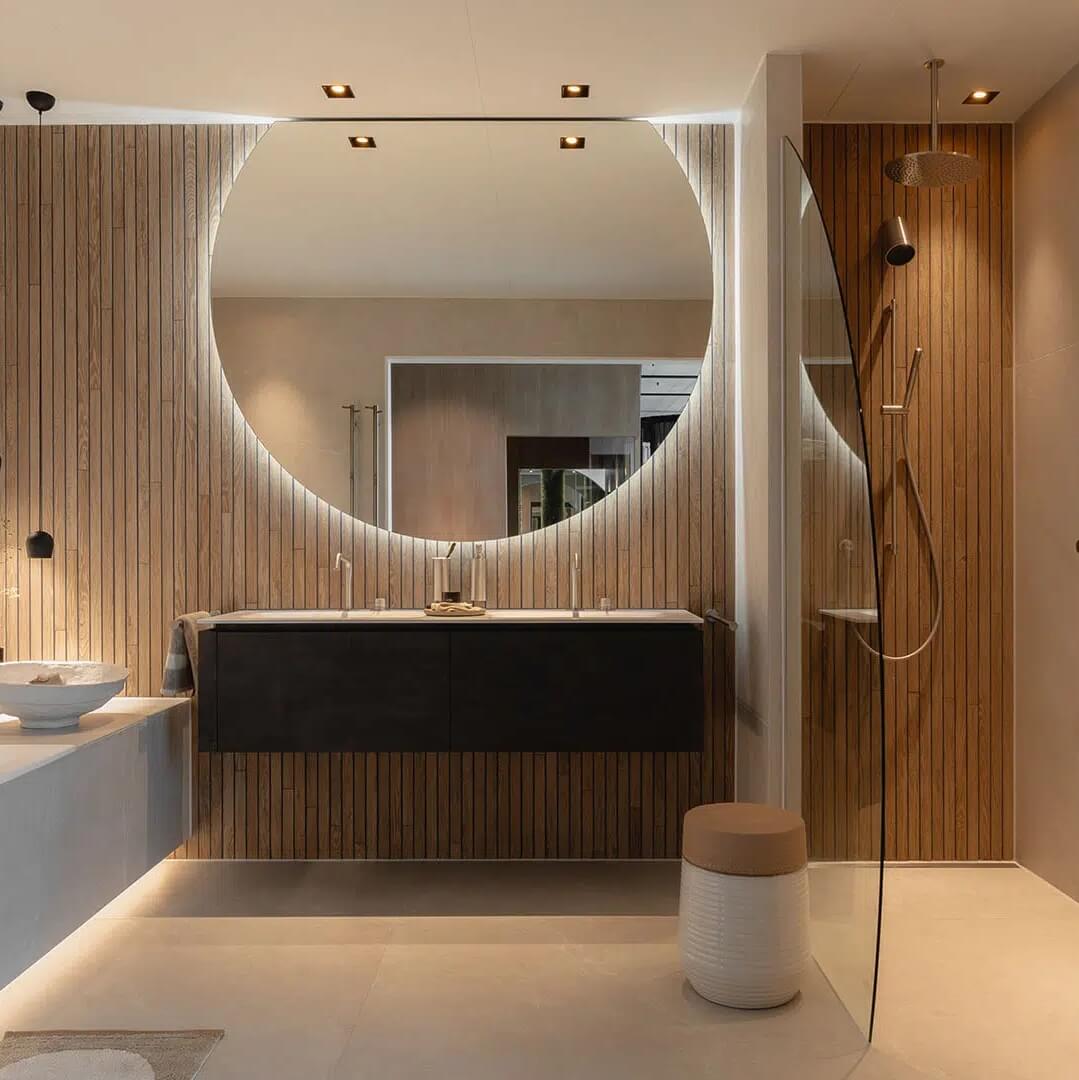 Luxe badkamer met houten wandpanelen, inloopdouche en ronde spiegel met verlichting